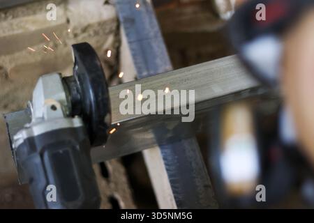 Worker with focused concentration uses hand tool for metal cutting work. This industrial angle grinder on steel bar creates bright hot spark during fa Stock Photo