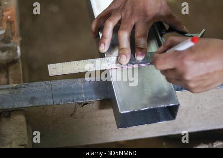 Close up of focused worker hand measuring and marking metal beam with square ruler. Diligent craftsman showing precision in construction and metalwork Stock Photo
