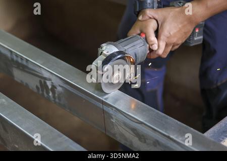 Focused worker uses an angle grinder to cut metal beam in workshop. This industrial fabrication work creates bright sparks, showing diligence, skill a Stock Photo