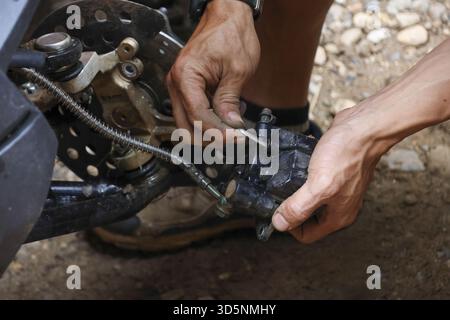 Focused man with dirty hands doing repair on vehicle suspension. mechanic using tool for maintenance on an off road machine, showing concentrated hand Stock Photo