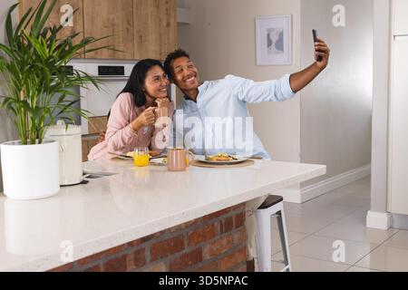 Couple enjoying breakfast at home, taking selfie with smartphone, smiling happily Stock Photo