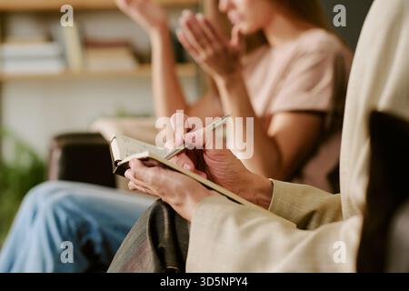 Caucasian Young Woman Gesturing While Psychologist Taking Notes during Session Stock Photo