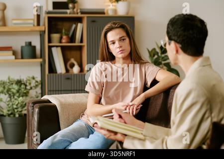 Young Caucasian Woman Sitting on Sofa Talking with Female Psychologist Stock Photo