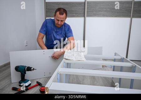 Man kneeling on floor, reading instructions and mounting new furniture with a screwdriver. Stock Photo
