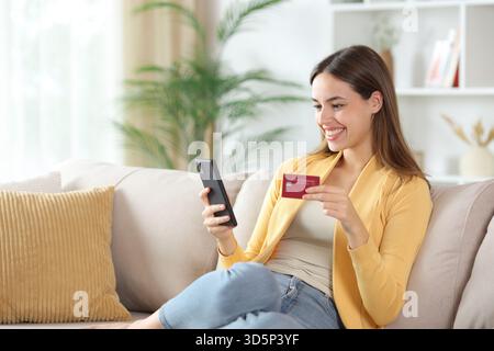 Happy woman in yellow buying online sitting on a couch at home Stock Photo