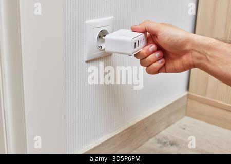 male hand insert a plug of the phone charger into socket at home Stock Photo