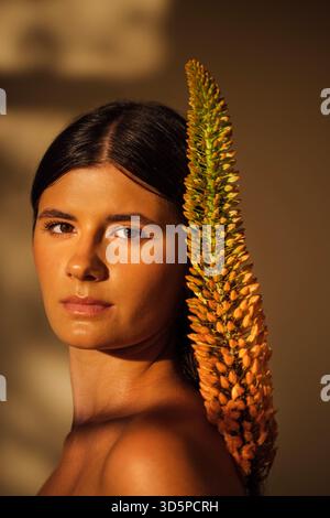 Dark-haired female model poses elegantly with a unique plant accent, highlighting her features and the interplay of light and shadow in a serene atmos Stock Photo