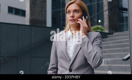 Serious confident Caucasian middle-aged business woman talking phone call near corporate office building businesswoman female entrepreneur specialist Stock Photo