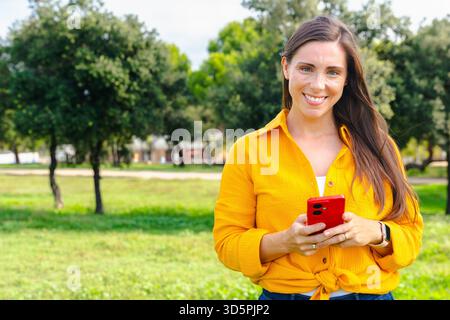 Smiling young woman using smartphone outdoors in park with copy space Stock Photo