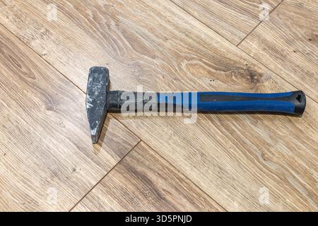 A blue nail hammer placed on the floor during renovation, vinyl plank flooring. Stock Photo