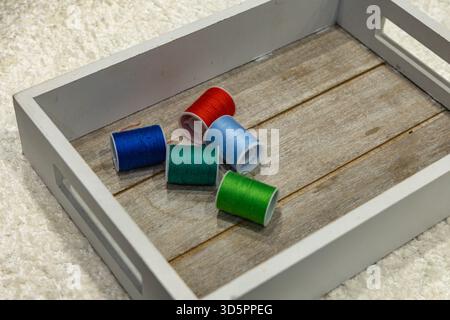 Pins with colorful sewing threads arranged in a wooden box on a table, colorful sewing threads Stock Photo
