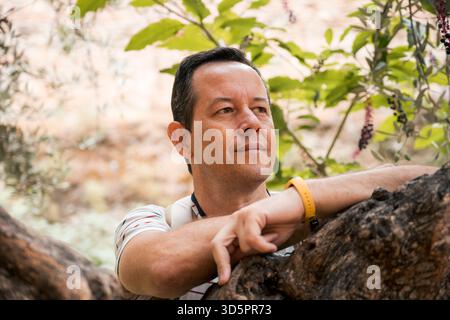 Thoughtful man leaning on tree in outdoor natural setting Stock Photo