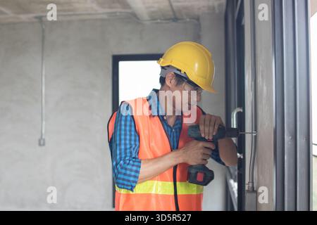 A construction worker is using a large,  hammer drill screwing  a screw into the wall using a cordless screwdriver Stock Photo