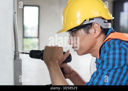 A construction worker is using a large,  hammer drill screwing  a screw into the wall using a cordless screwdriver Stock Photo