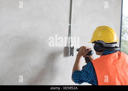 A construction worker is using a large,  hammer drill screwing  a screw into the wall using a cordless screwdriver Stock Photo
