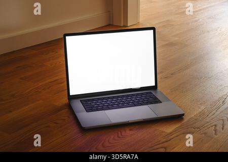 Open laptop with blank white screen placed on wooden floor in warm interior light, minimal workspace or design mockup concept. Selective focus. Stock Photo