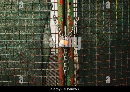 Security concept with padlock and chain locking wire fence in daylight. Selective focus. Stock Photo