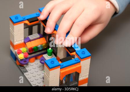 A child's hand adds the finishing touch to a vibrant Lego creation on a table. Stock Photo