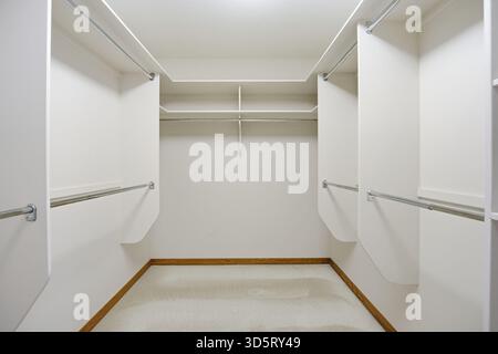 Large walk in closet with white walls and shelves. The closet is empty and has no clothes hanging on the racks Stock Photo