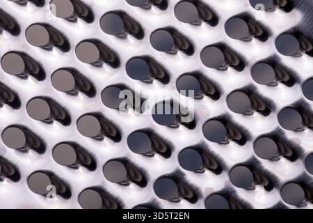 Macro view of a shiny metal grater with round holes and textured pattern. Abstract industrial background with metallic reflections. Stock Photo