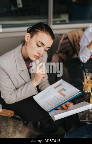 Businesswoman reviewing charts and graphs while contemplating at a coffee table Stock Photo
