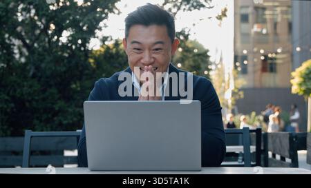 Happy excited Asian business man winning with laptop rejoice looking computer Korean businessman win achieve victory online internet job working in Stock Photo