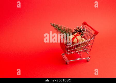 Mini cart with wrapped gifts and pine cones on a bright red background with wide copy space Stock Photo