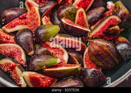 A bowl of black and green figs. The bowl is full of figs, some of which are cut in half. The figs are ripe and ready to eat Stock Photo