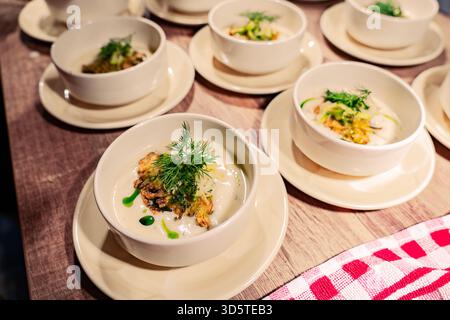 A table with several white bowls of food on plates. The bowls are filled with different types of food, including soup and salad. The table is set for Stock Photo