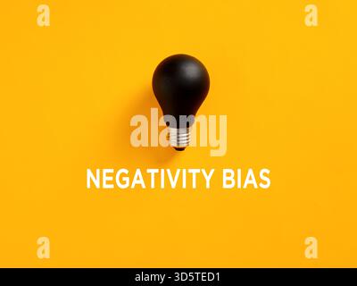 Negativity bias concept illustrated by a black light bulb on a yellow background, representing pessimism and lack of ideas Stock Photo