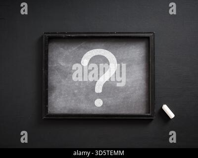 White question mark drawn on a small chalkboard with chalk on black background representing frequently asked questions, education and problem solving Stock Photo