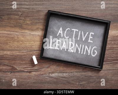 Small chalkboard with active learning written on it and a piece of chalk lying on a wooden desk. Stock Photo
