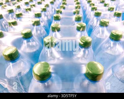 Multiple plastic water bottles tightly packed in shrink wrap, seen from above. Green caps, blue-toned bottles, clean, fresh visual, hydration, mass Stock Photo