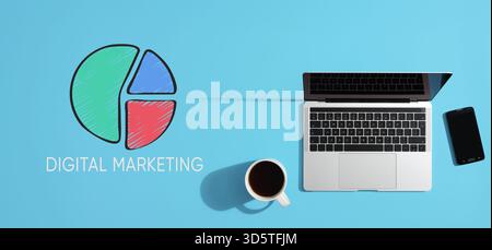 Top view of a laptop, smartphone and a cup of coffee on a blue desk, with a pie chart representing digital marketing strategy Stock Photo