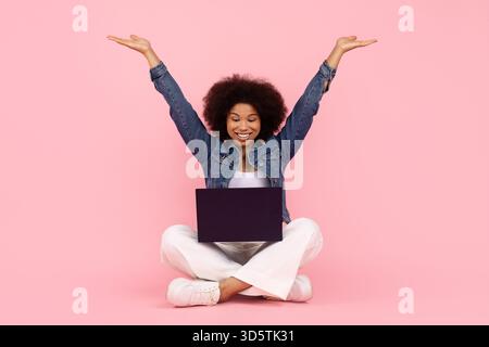 Happy African American woman raising arms in excitement while using laptop Stock Photo