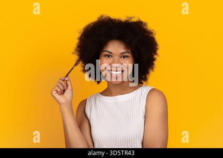 Charming black woman smiling and playing with her curly hair strand Stock Photo