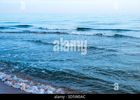 Serene Ocean Waves Rolling Onto a Quiet Beach Under a Pale Blue Sky Stock Photo