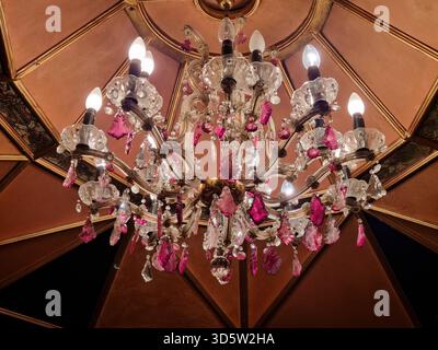 Close up of luxurious vintage crystal chandelier with pink pendants under a wooden ceiling with geometric patterns Stock Photo