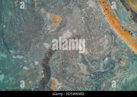 Top-down abstract photograph of industrial tailings or chemical runoff. Unnatural swirling patterns of blue-gray, turquoise, and rusty orange minerals - environmental pollution and contamination. Stock Photo