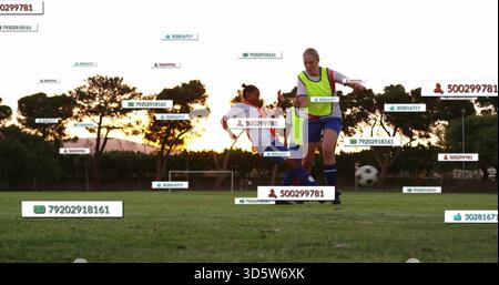 Playing players in neon vests sliding, controlling ball on school field at sunset with ID labels Stock Photo