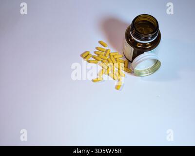 Yellow Capsules Spilled from Bottle - Bright yellow medical capsules, marked A155 and 10, are scattered from an open amber glass bottle on a pristine Stock Photo