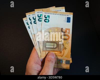 Hand Holding Fifty Euro Banknotes - Close-up of a hand holding and fanning out multiple 50 Euro banknotes against a dark background. Symbolizes financ Stock Photo