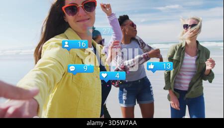 Taking woman in yellow jacket holding smartphone for selfie at ocean beach, with reaction overlays Stock Photo