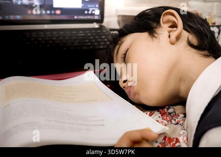 Southeast Asian boy fallen asleep while doing his homework on a computer at home after school Stock Photo