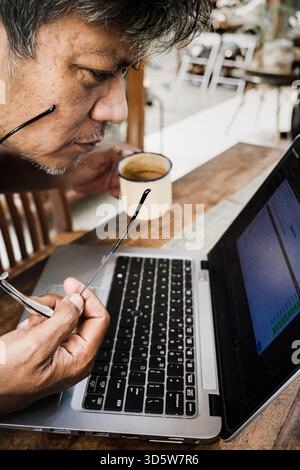 Asian adult male person concentrating and looking serious while working from home on a notebook computer. Remote work concept. Stock Photo