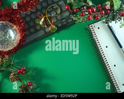 Christmas Workspace with Decorations - Flat lay of Christmas decorations, a keyboard, notebook, and pen on a vibrant green background, offering ample Stock Photo