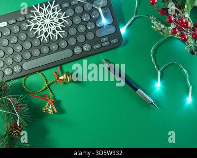 Festive Work Setup with Keyboard - Flat lay of a computer keyboard adorned with Christmas decorations and fairy lights on a vibrant green background, Stock Photo