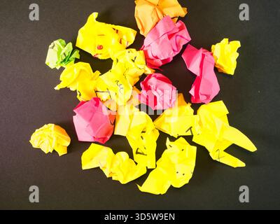 Crumpled Colorful Paper Pile - Heap of brightly colored, crumpled papers, including yellow, pink, and orange, on a black surface. Ideal for themes of Stock Photo