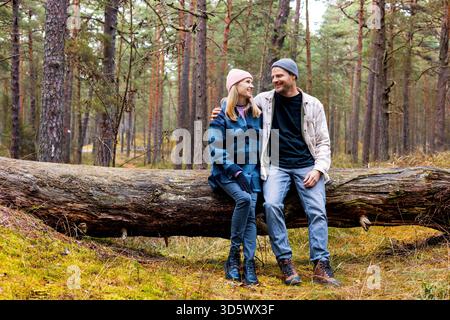smiling couple sitting and resting on fallen tree after walk in autumn park Stock Photo