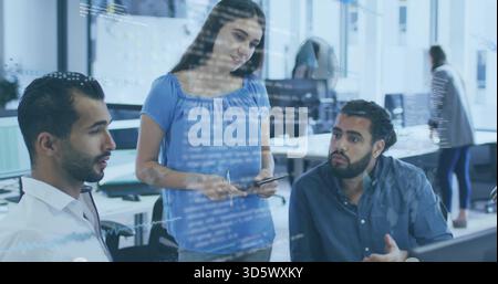 Explaining woman in blue blouse pointing to tablet between two seated men in office, code overlay Stock Photo